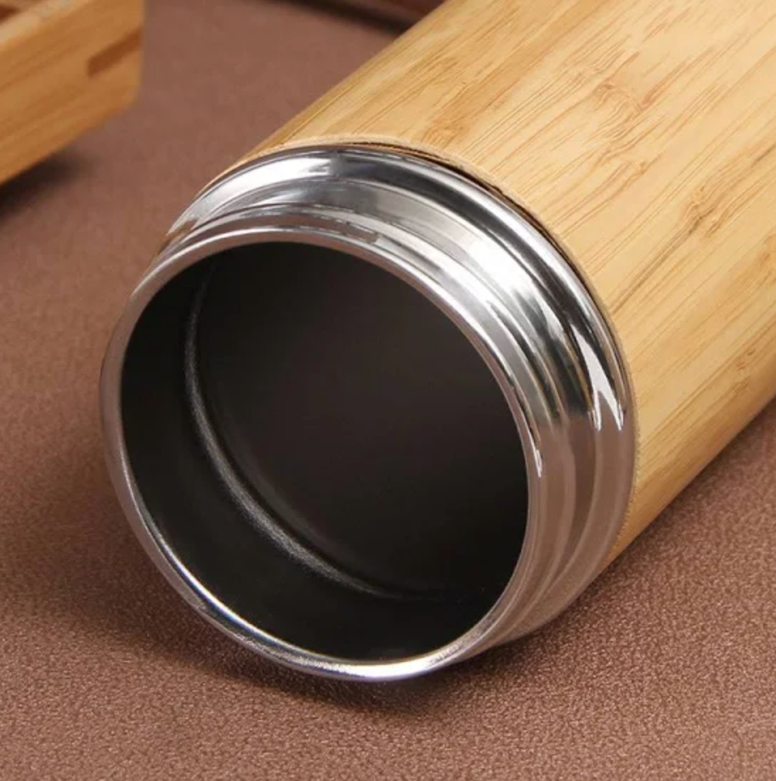 Bamboo water bottle with a silver rim on a brown surface