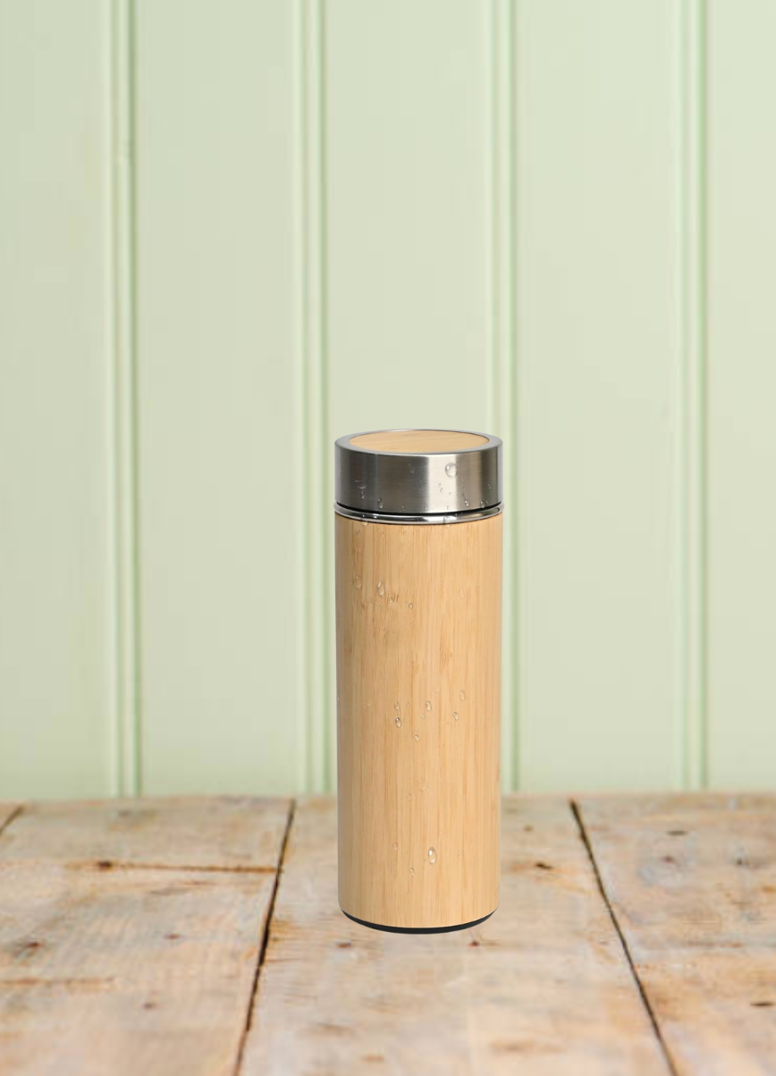 Bamboo water bottle with steel lid on a wooden surface against a light green wall