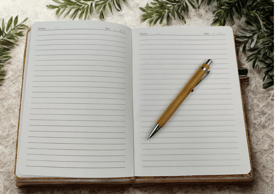 Open notebook with a pen on a textured surface with greenery