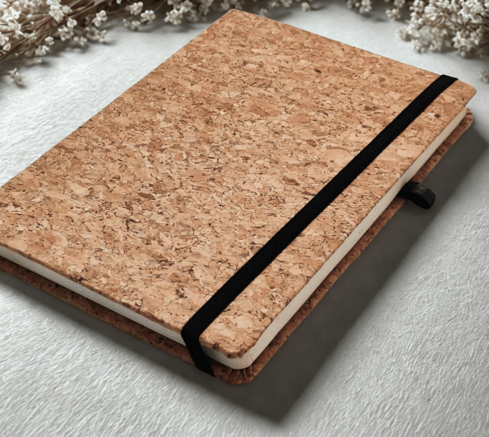 Cork notebook with a black strap on a light gray surface with dried flowers in the background