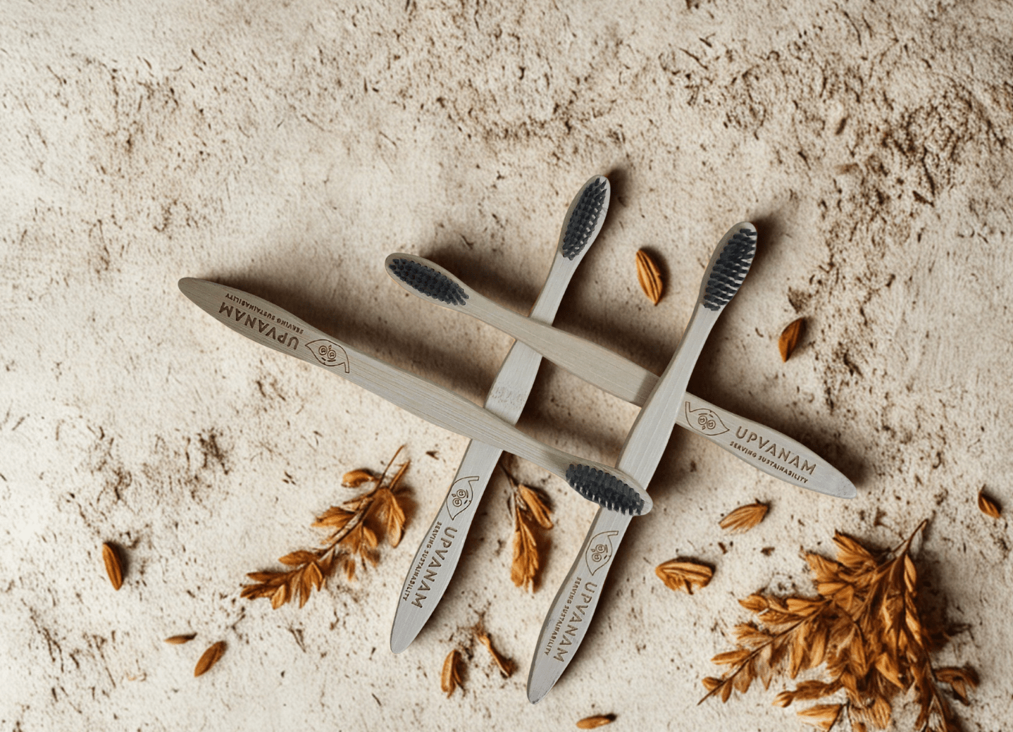 Set of four Upvanam toothbrushes on a textured surface with dried leaves.