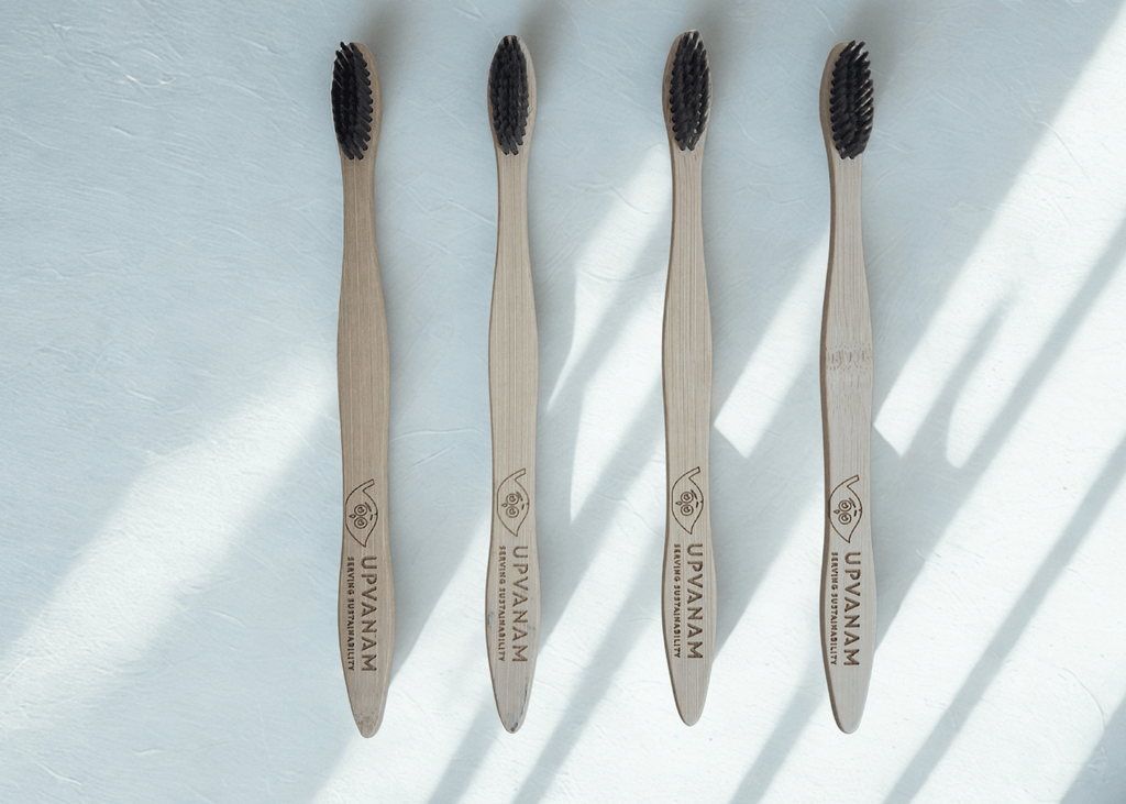 Four bamboo toothbrushes with black bristles on a light surface