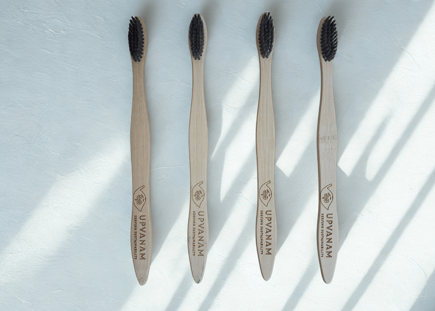 Four bamboo toothbrushes with black bristles on a light surface